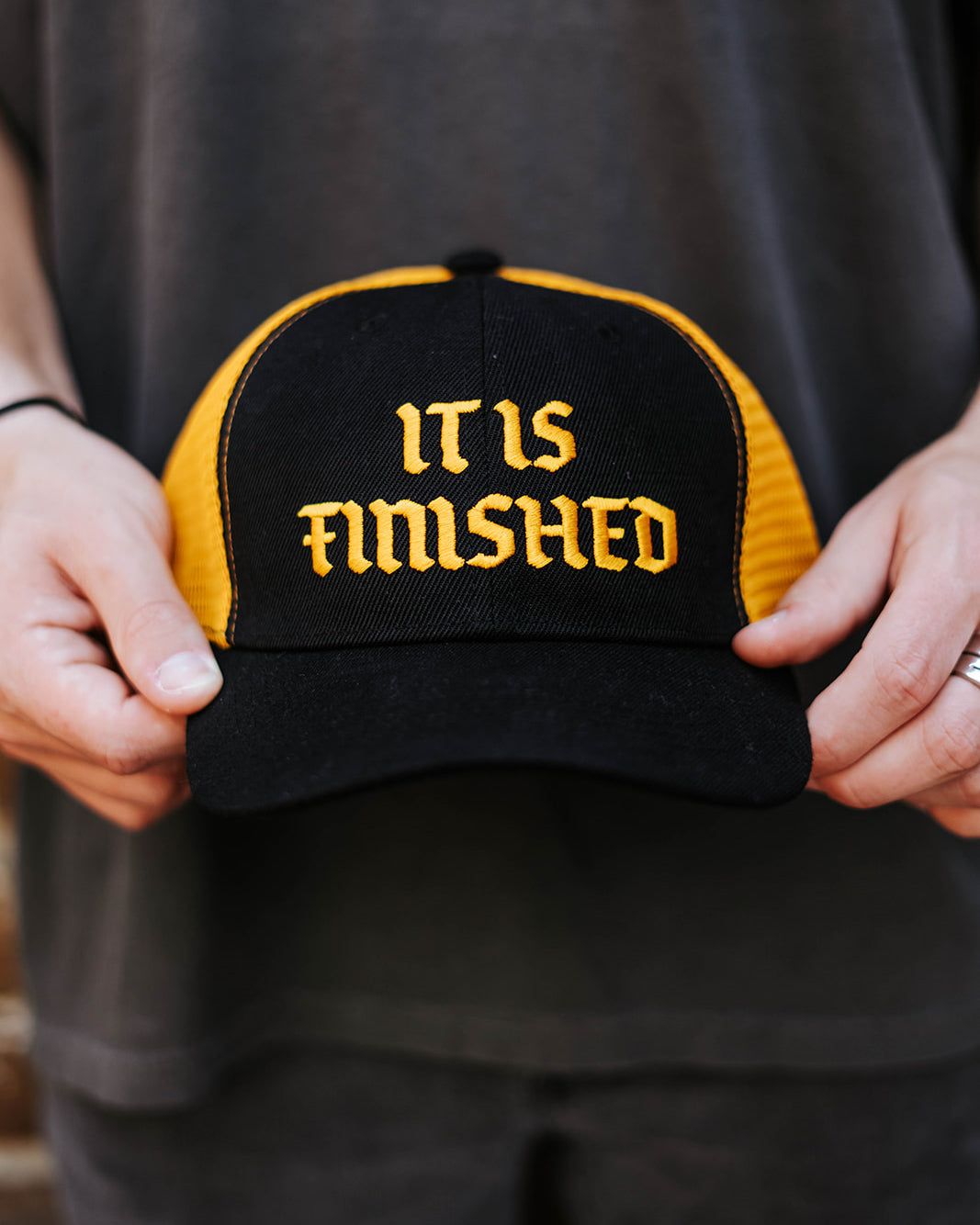Gorra snapback negra y amarilla con la frase "It Is Finished"